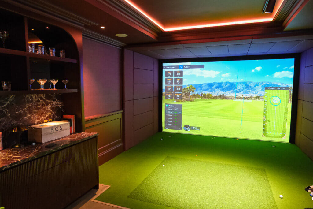 Private golf simulator bay with a large impact screen, hitting turf and a bar
